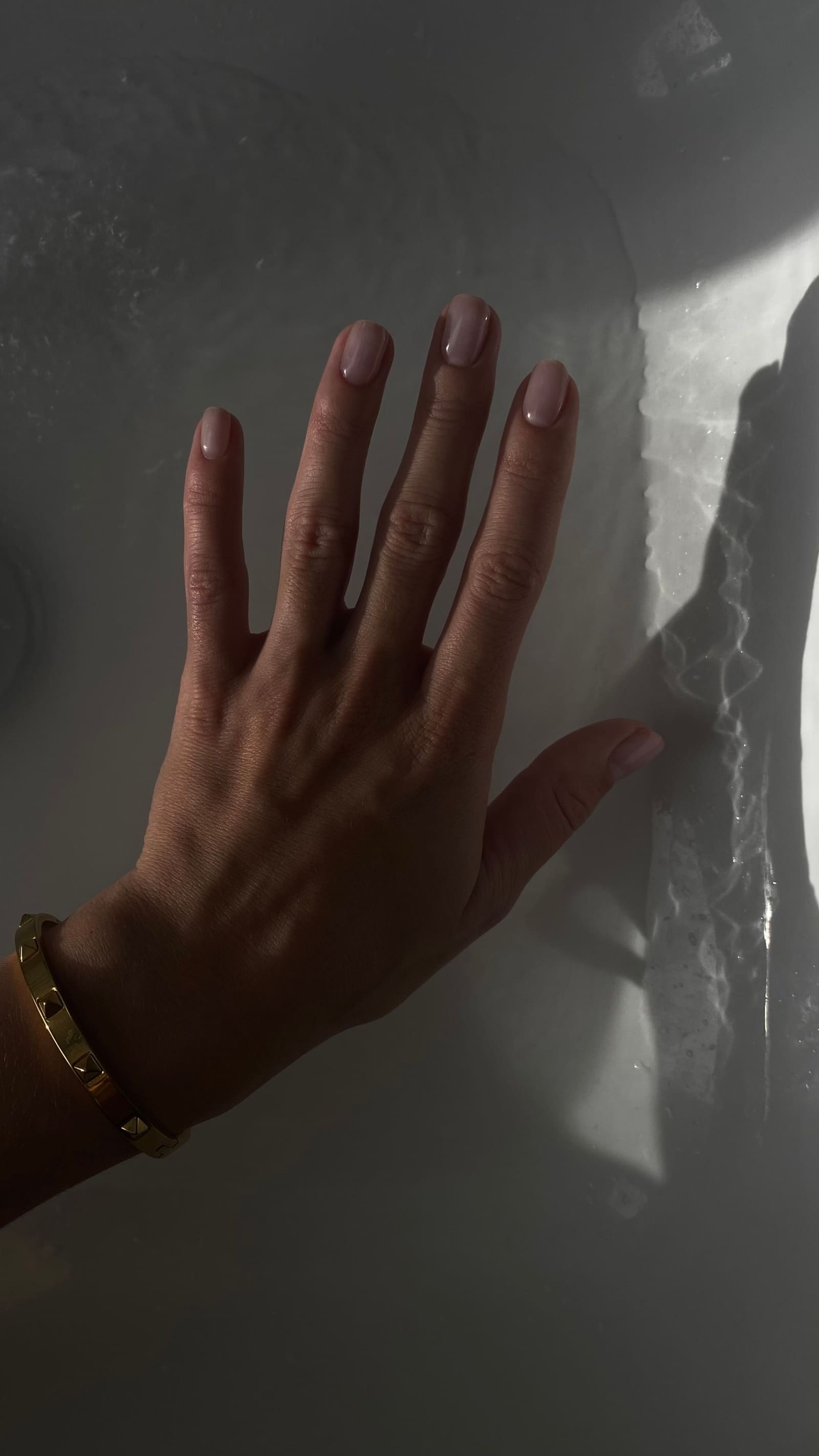 Bare nails and a gold bangle in soft light